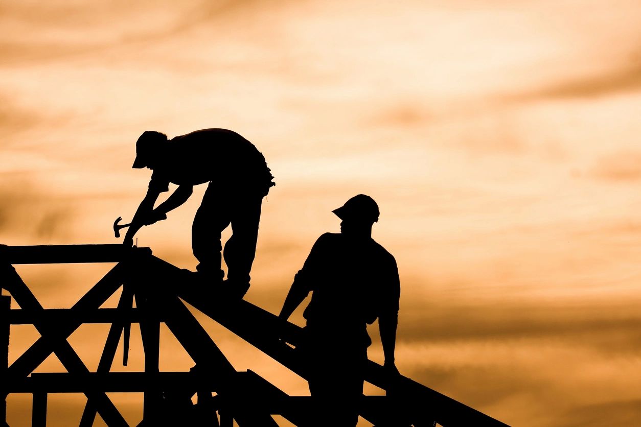 Silhouette of two workers on roof at golden sunset